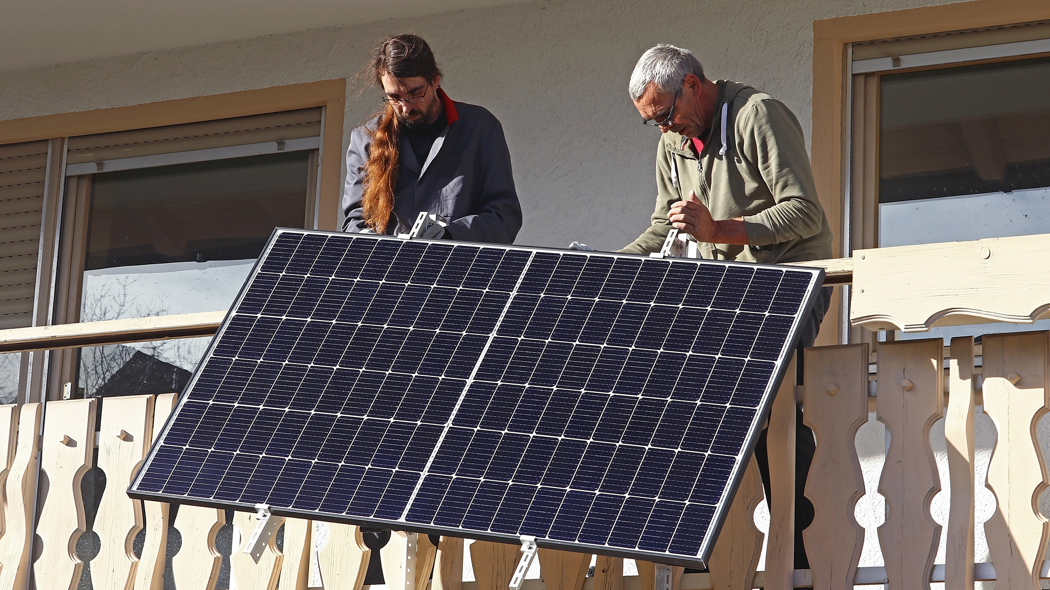 Zwei Männer montieren Solarpanels auf einem Balkon.