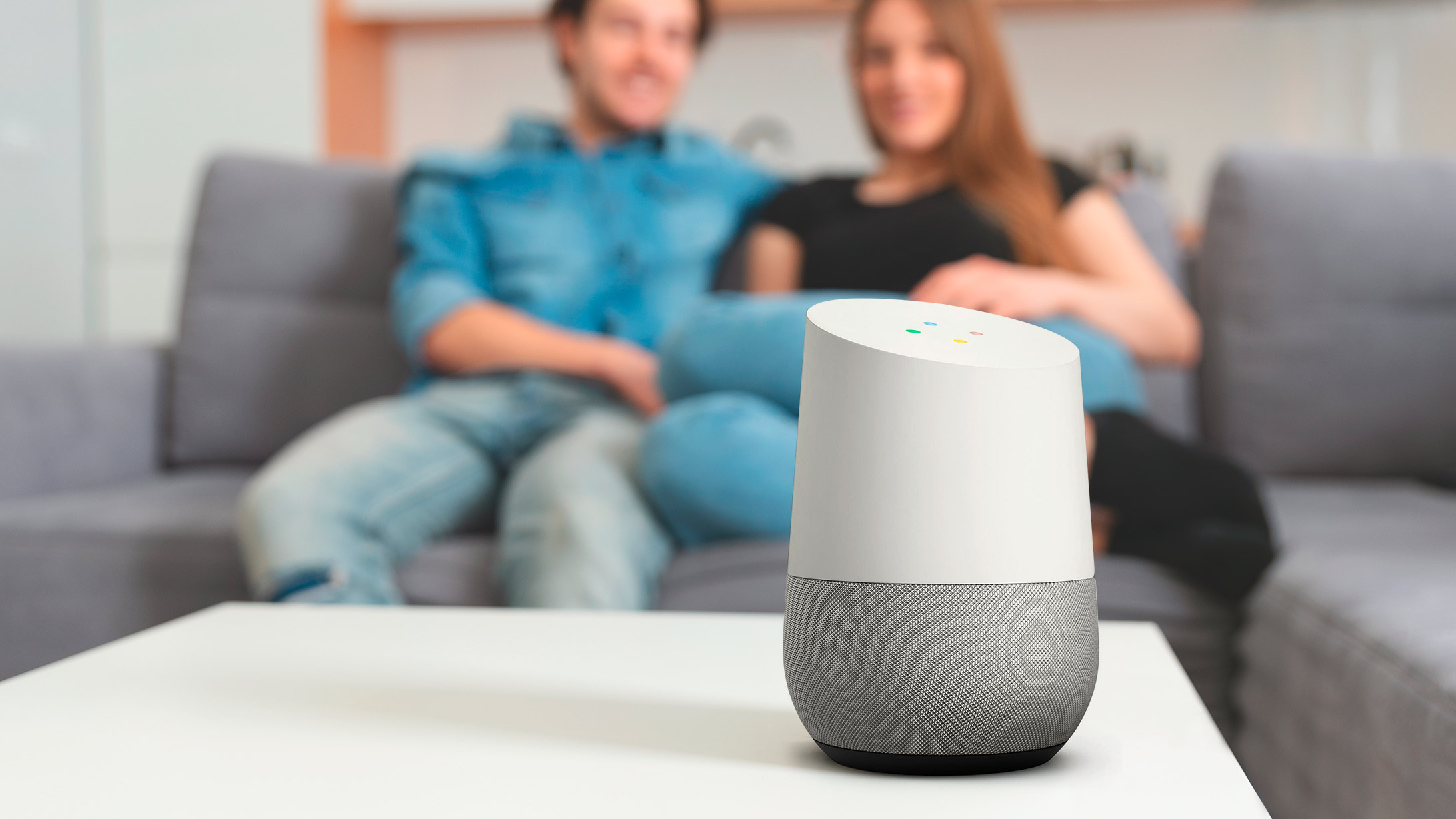 Google Home Smart Speaker mit zwei Menschen im Hintergrund