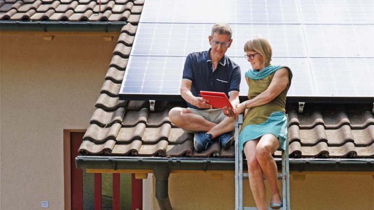 Simone und Philipp Matter mit einem Tablet auf ihrem Dach vor der Photovoltaik-Anlage mit Solaranlage