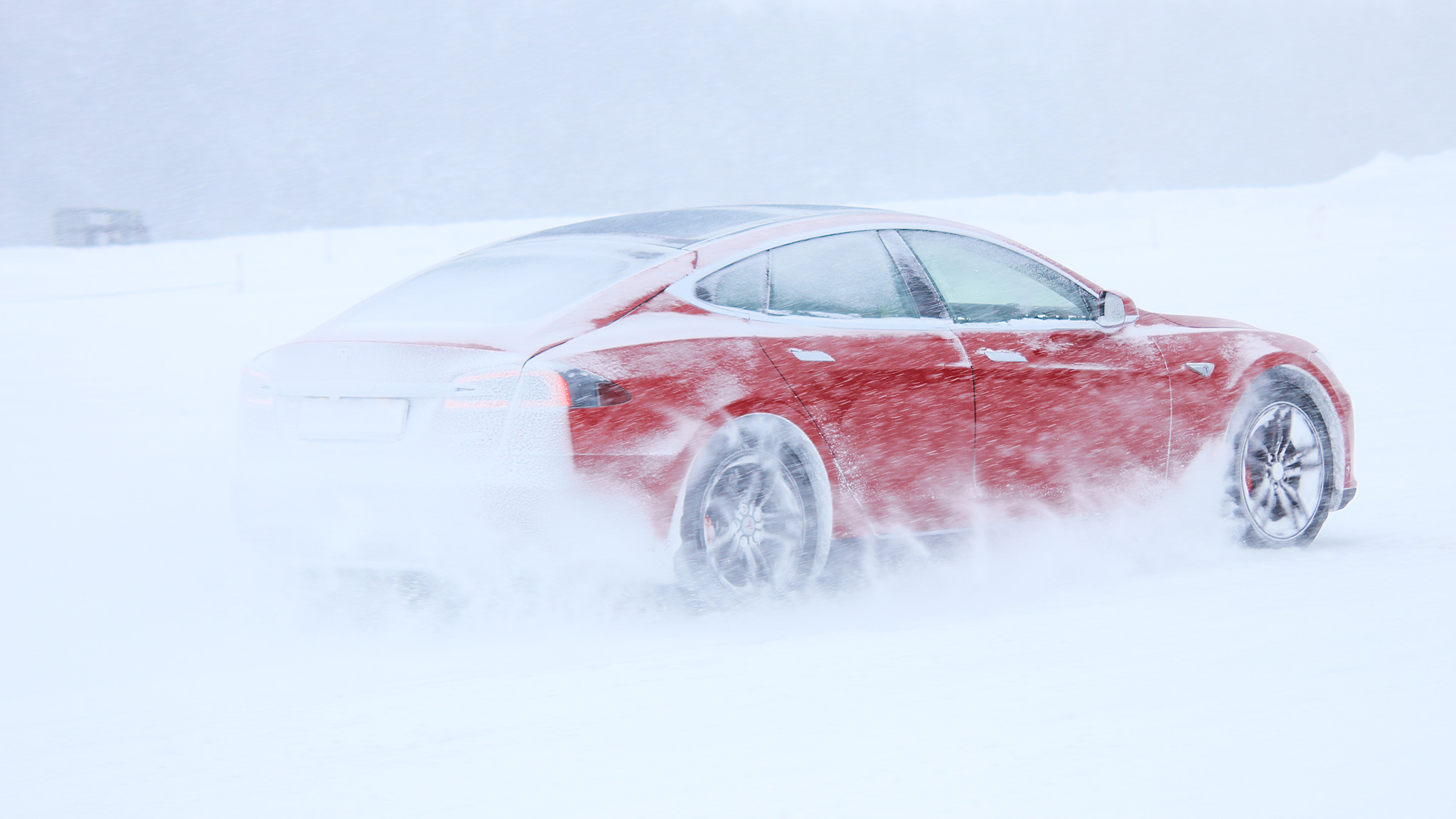 Rotes Tesla-Elektroauto fährt im Winter durch Schnee-Gestöber