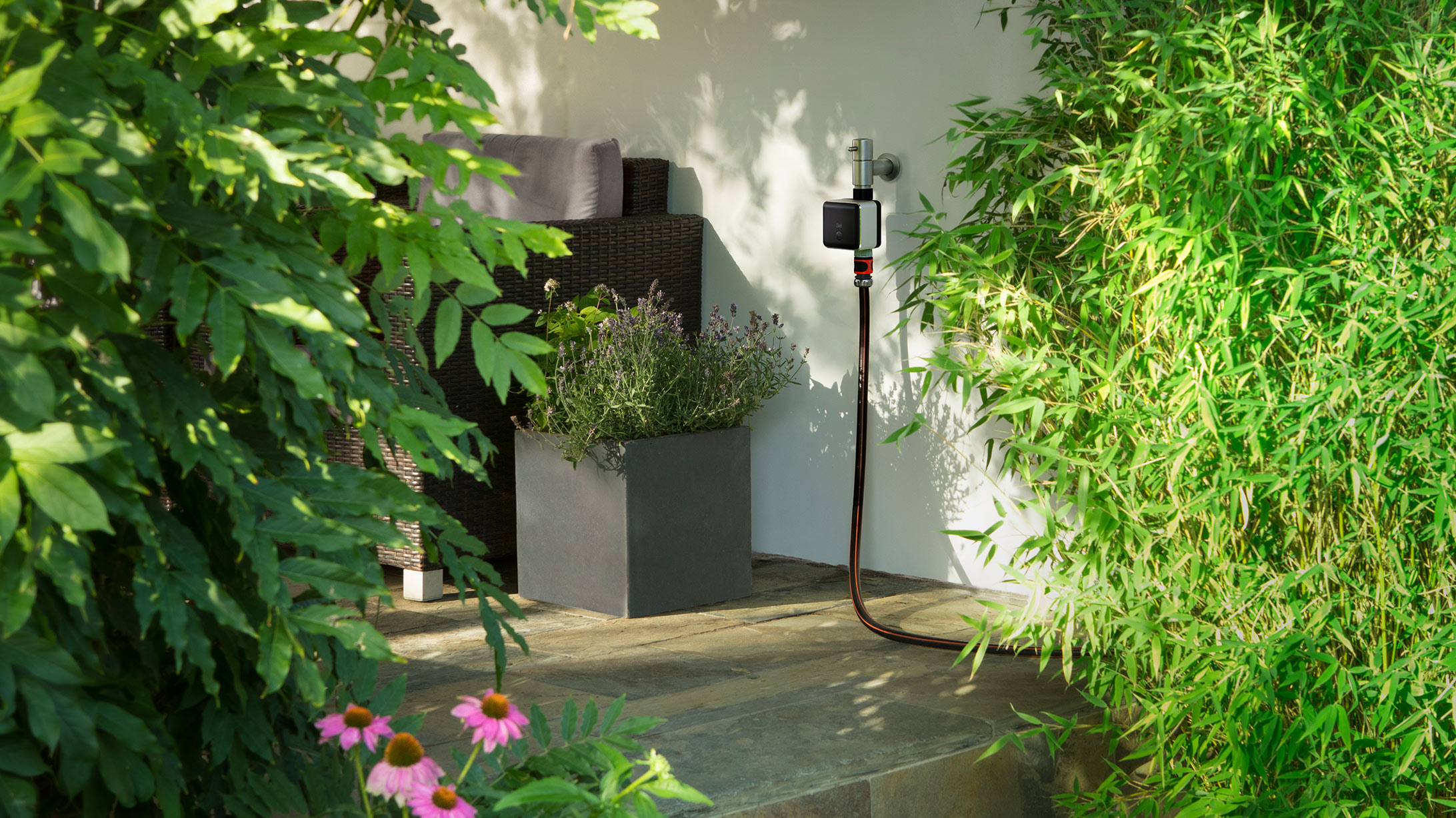 Der Bewässerungscomputer Eve Aqua ist an einer Wasserleitung in einem grünen Garten montiert.