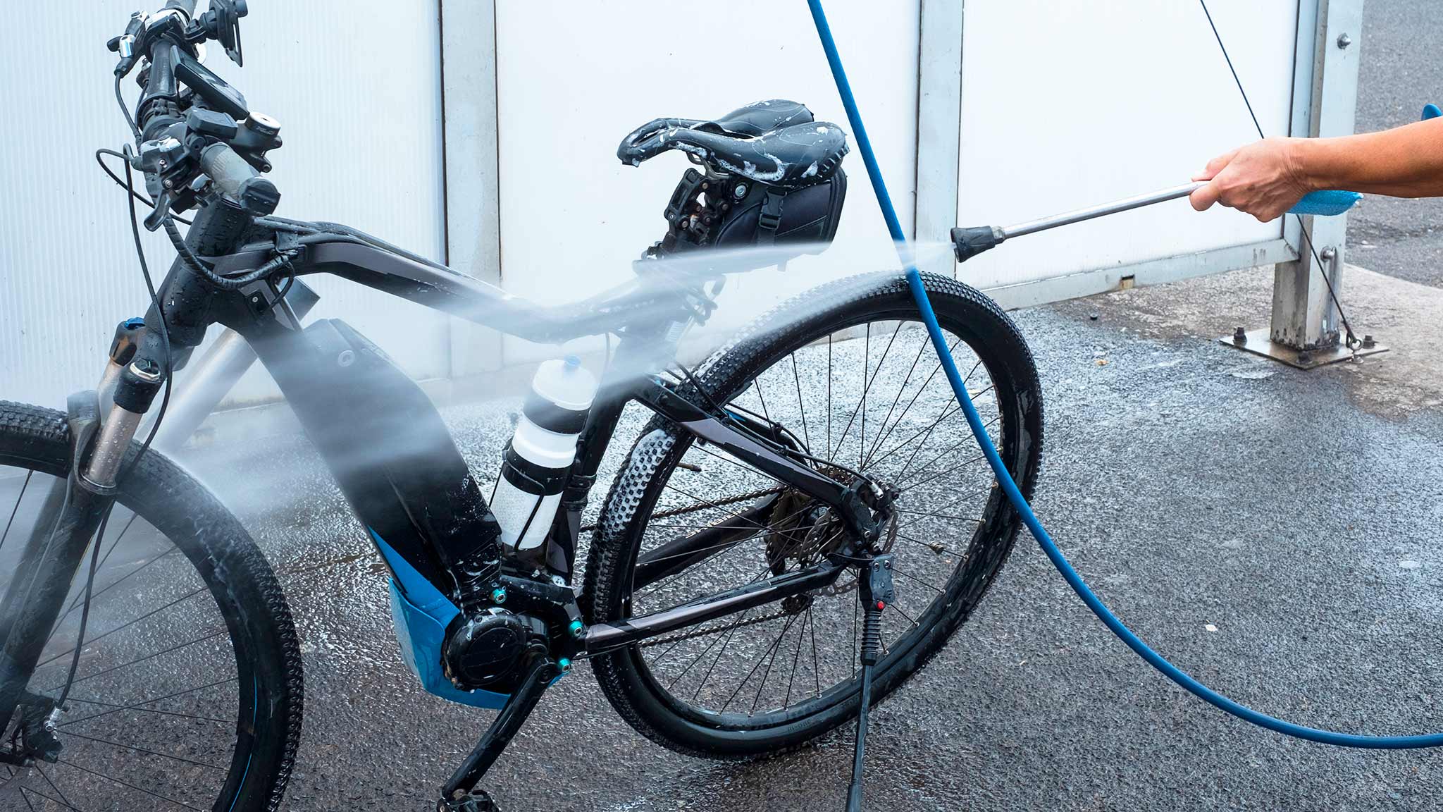 Eine Person spritzt im Winter mit einem Hochdruckreiniger auf ein E-Bike