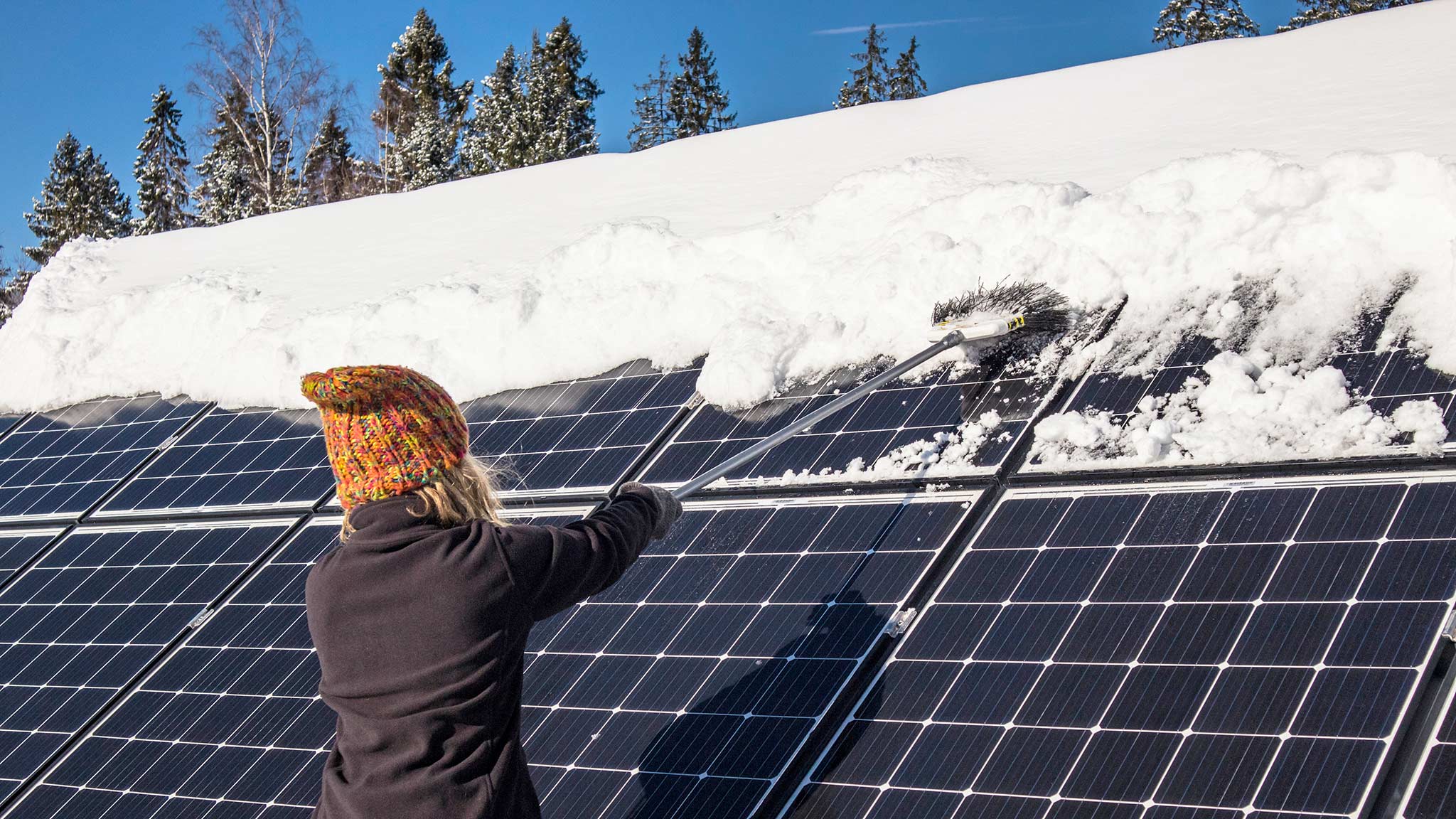 Frau entfernt mit einem Besen Schnee von einer Solaranlage