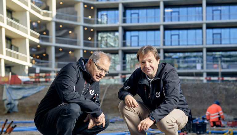 Martin Dietler, Leiter Wärmeprojekte, und Roland Bürgin, Projektleiter Wärme bei Primeo Energie in der Hocke auf dem Baselink-Areal.
